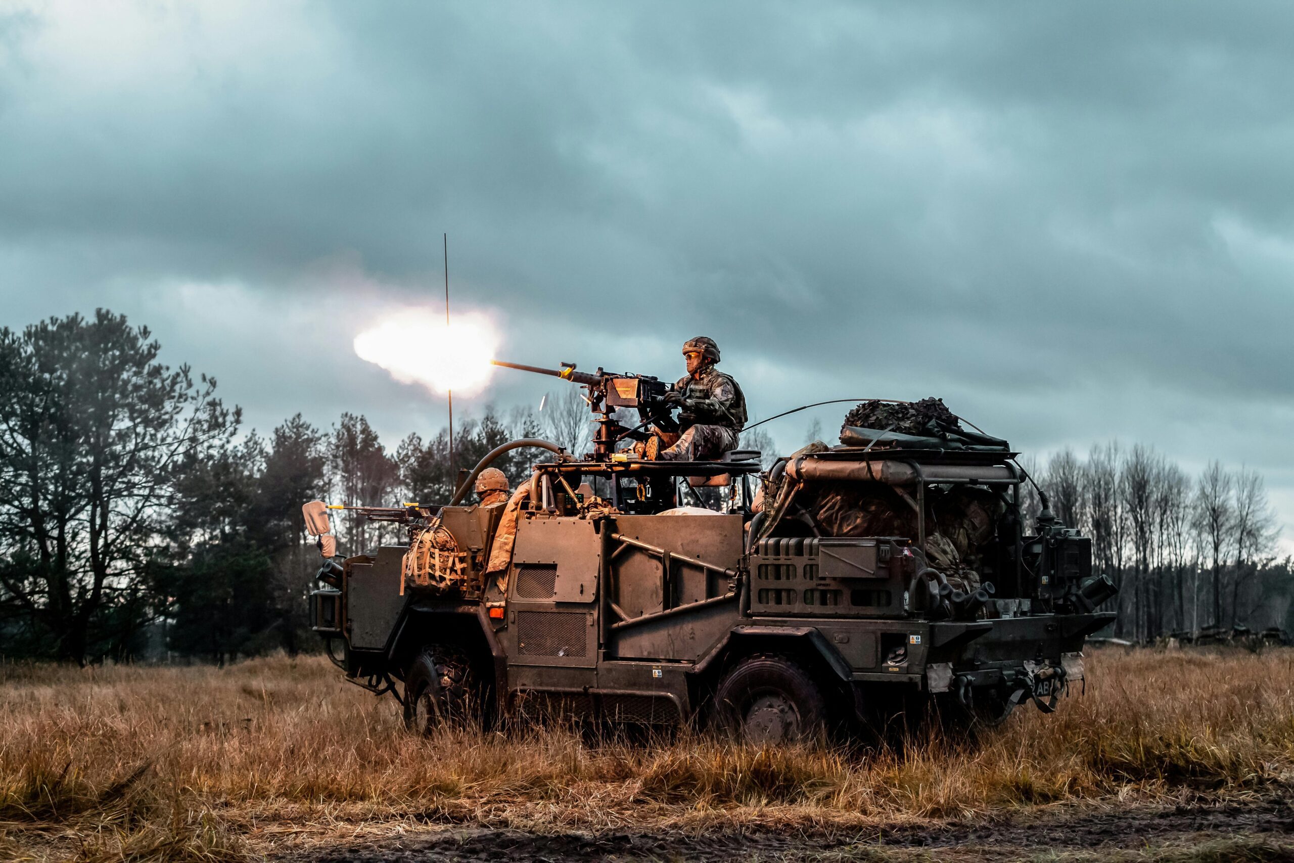 A soldier operates a mounted weapon on a military vehicle in an open field, showcasing a modern military exercise.