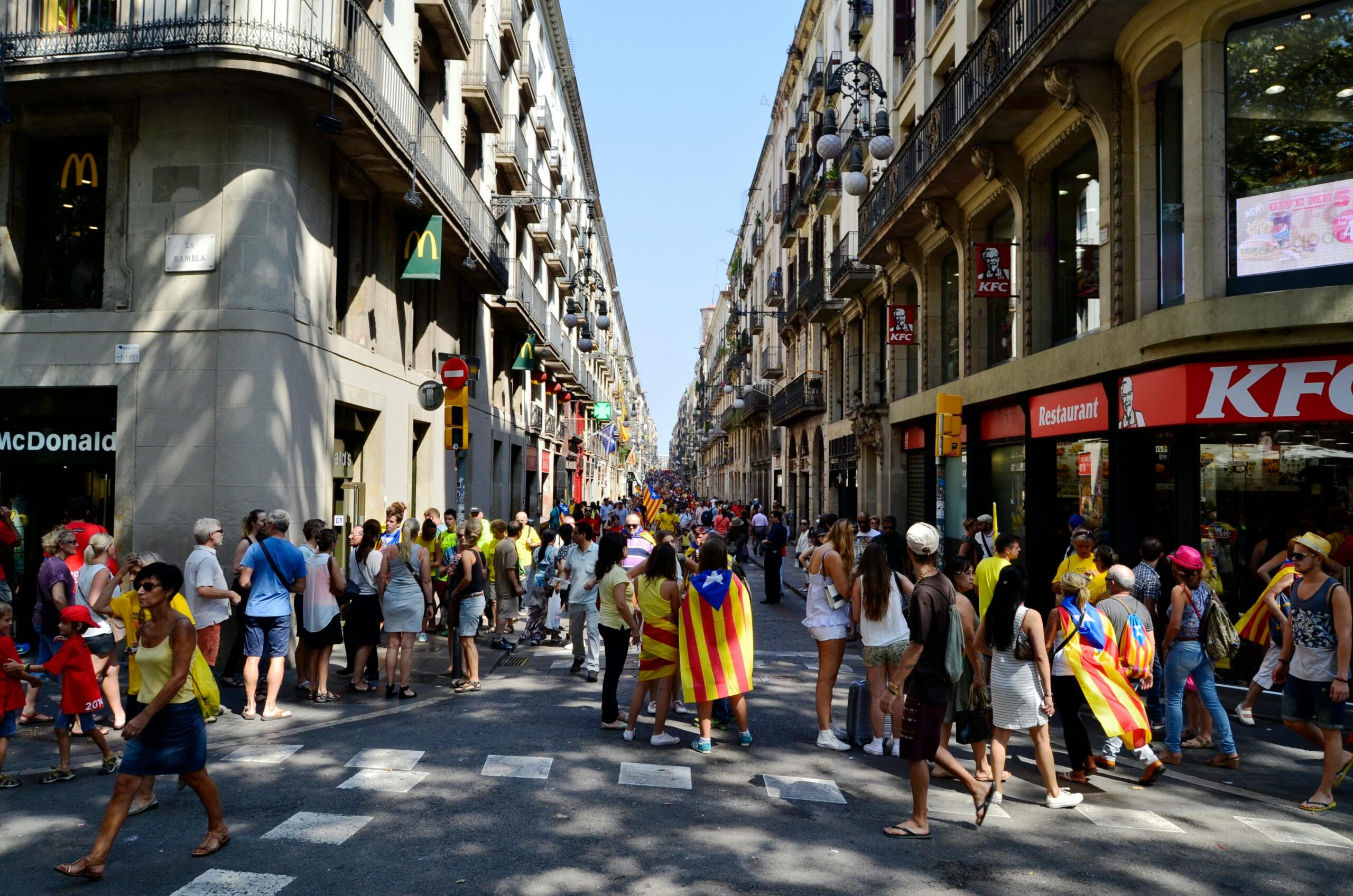 Busy street in Barcelona with a diverse crowd displaying Catalan flags and urban lifestyle.