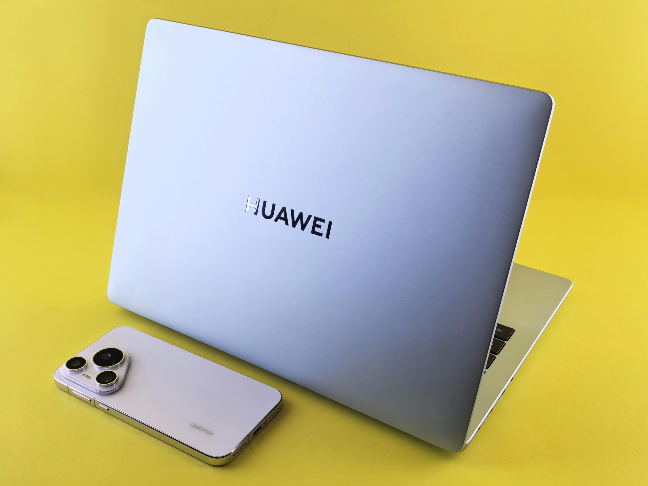Silver laptop and smartphone on a bright yellow surface, showcasing modern technology.