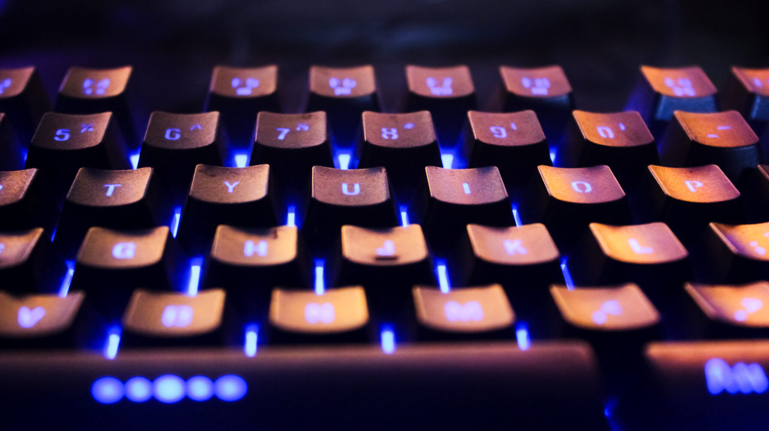 Vibrant close-up of a backlit computer keyboard in a dark setting with glowing blue lights.