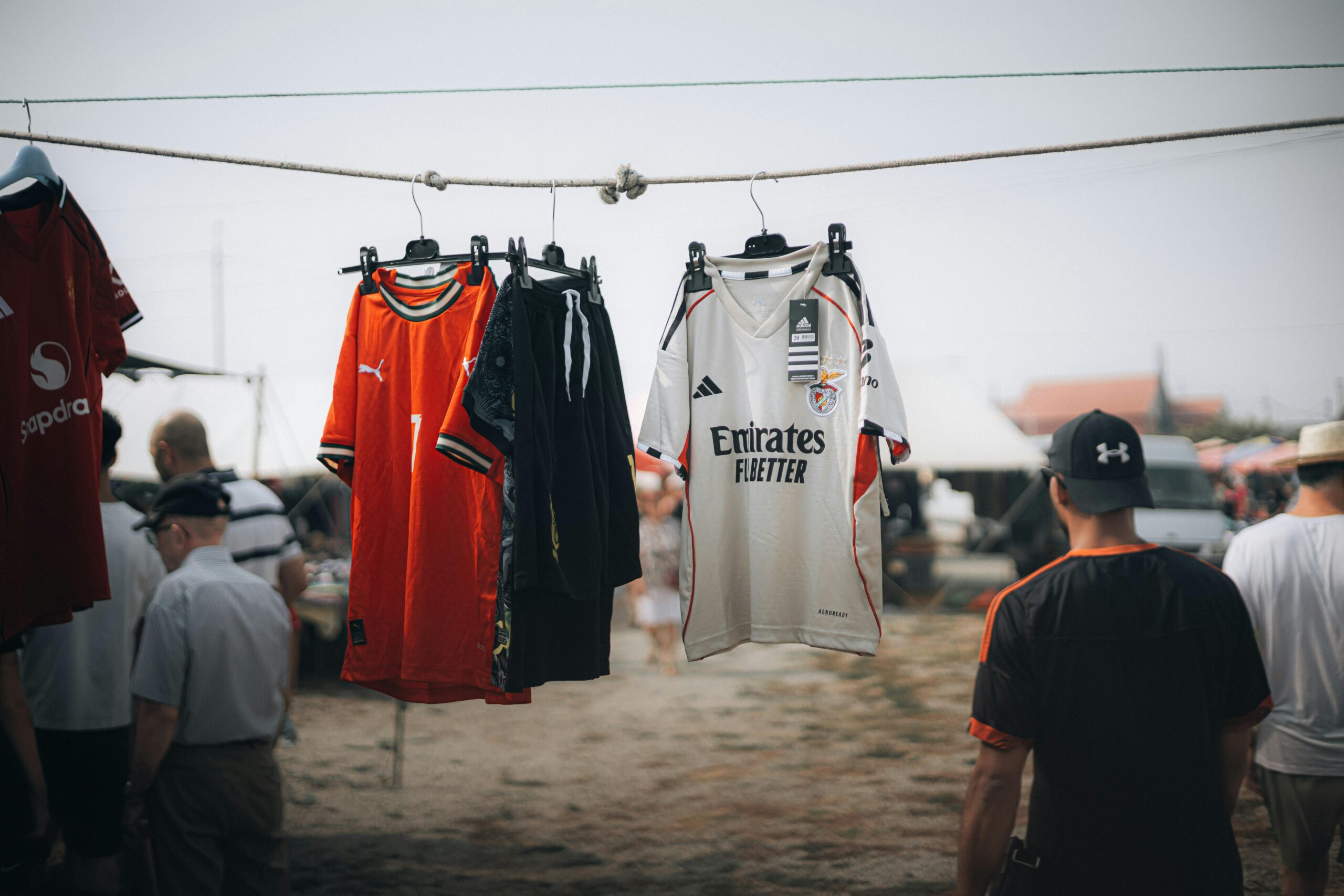 Colorful sports jerseys hanging at an outdoor market with people in the background.