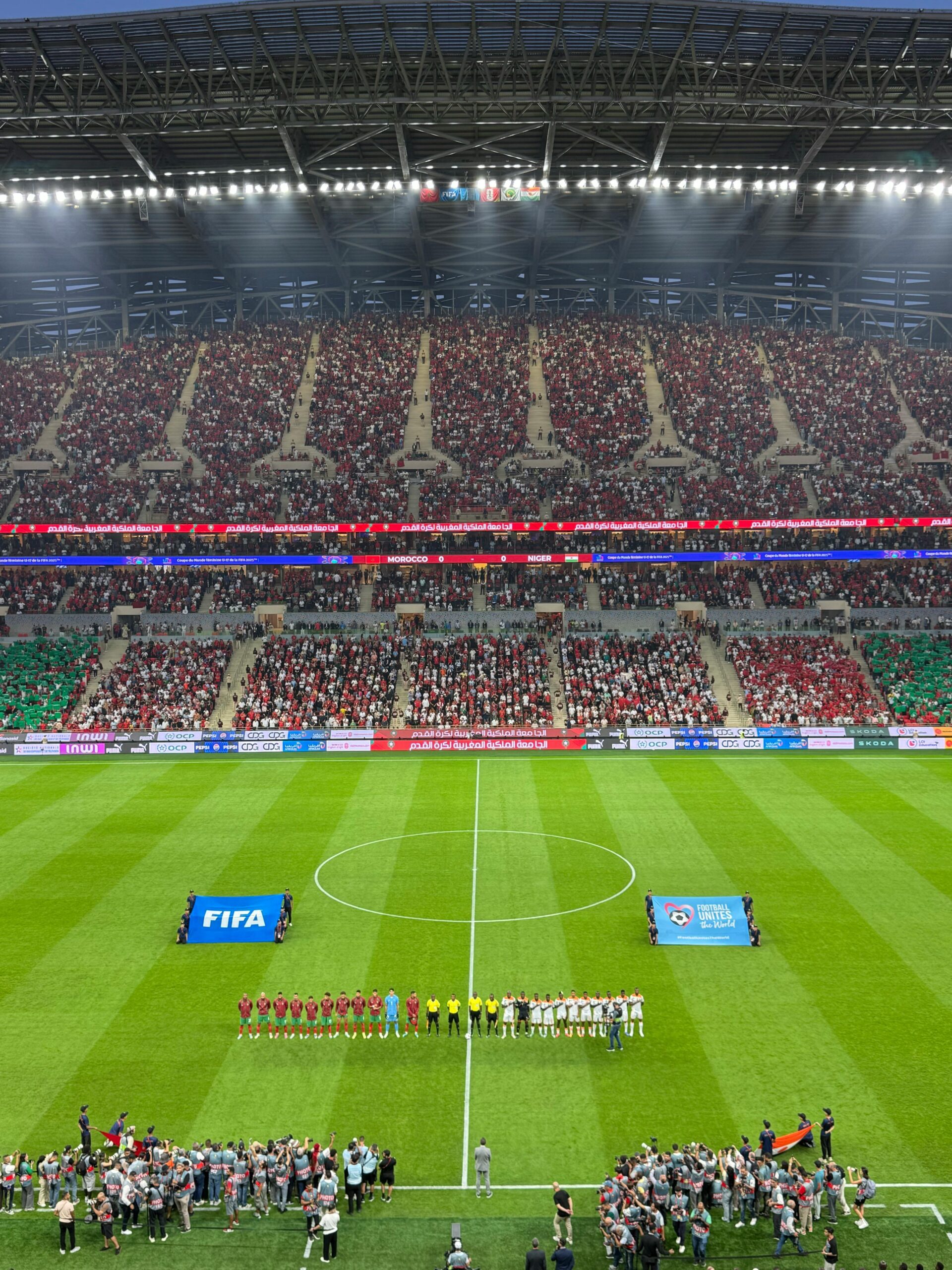 Aerial view of a football match kickoff in a vibrant, full stadium.