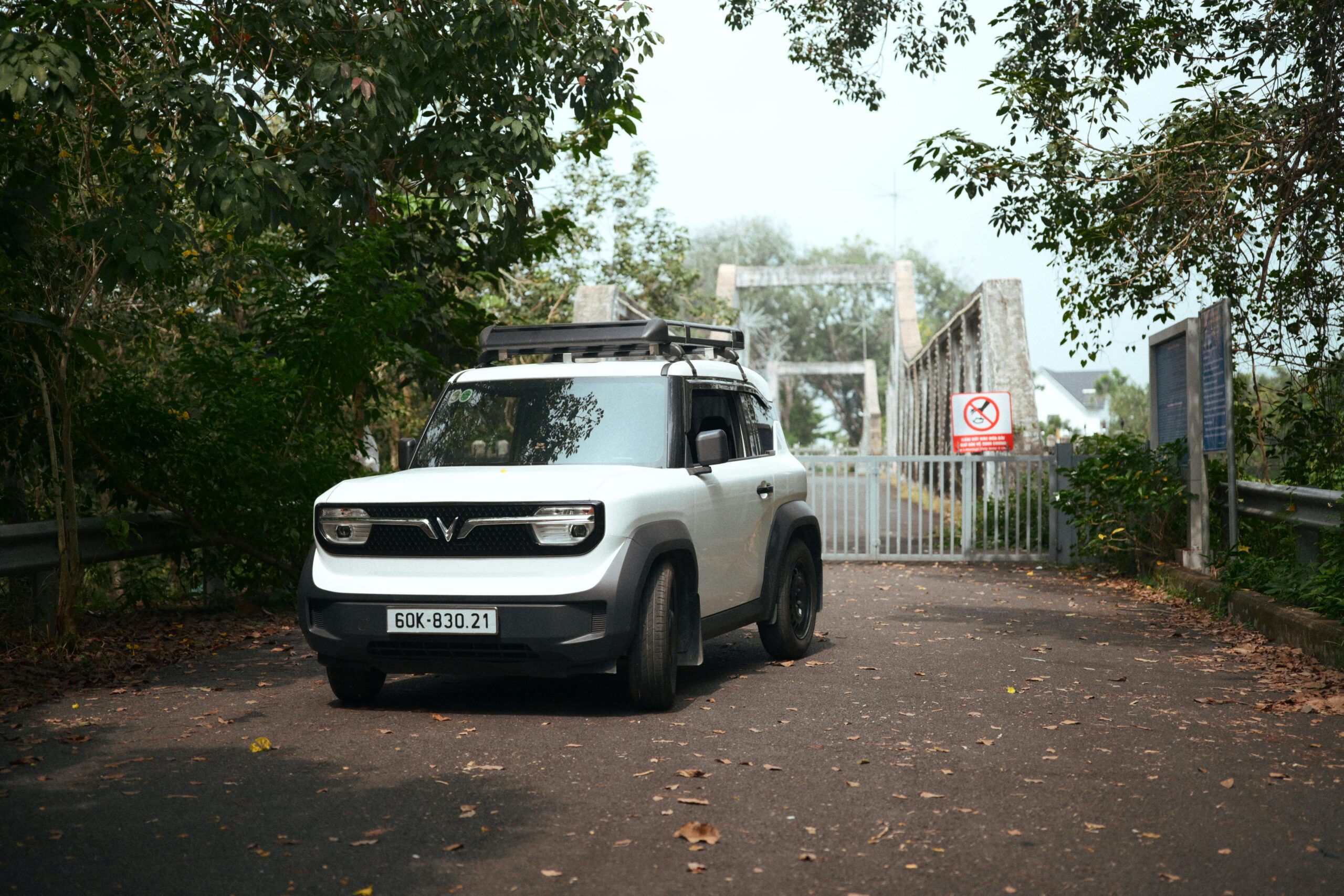 White SUV parked near a gated road surrounded by dense greenery and trees.