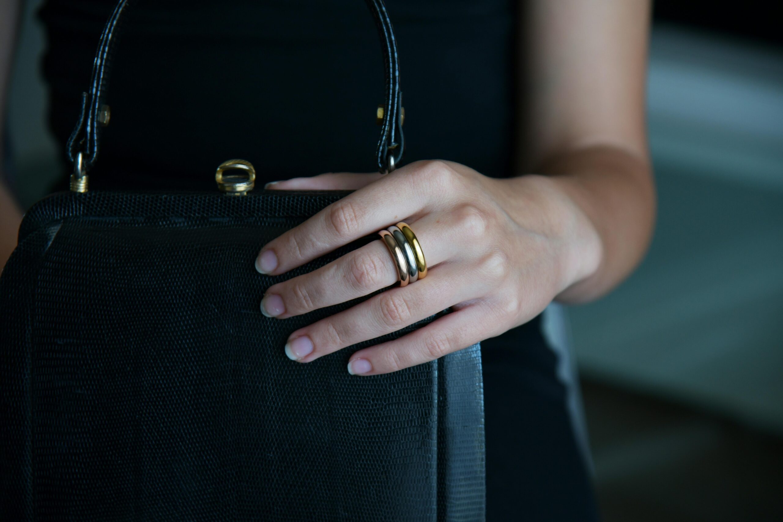 Close-up of a woman's hand with a gold ring holding a black handbag, showcasing elegant fashion accessories.