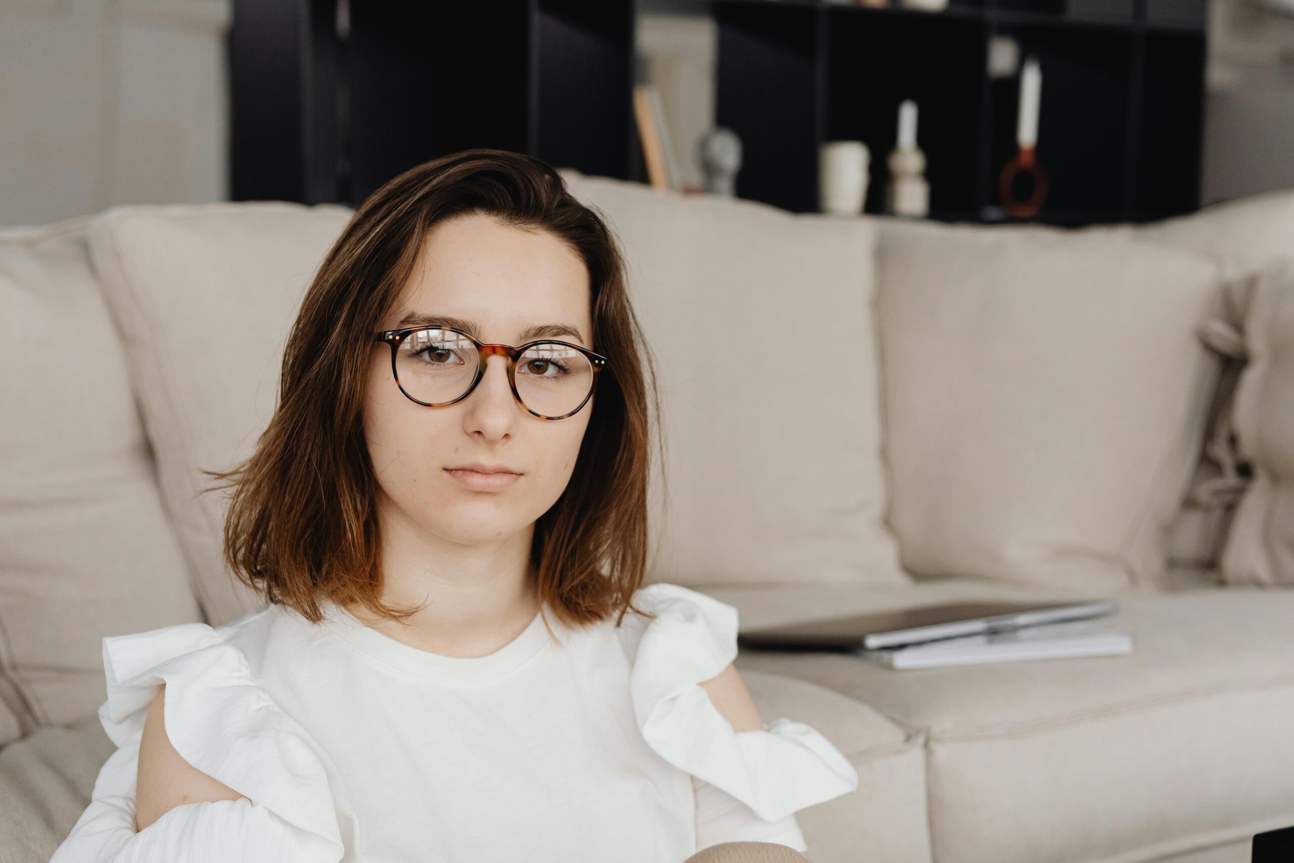 Portrait of a woman with eyeglasses in a casual setting, wearing a white blouse.