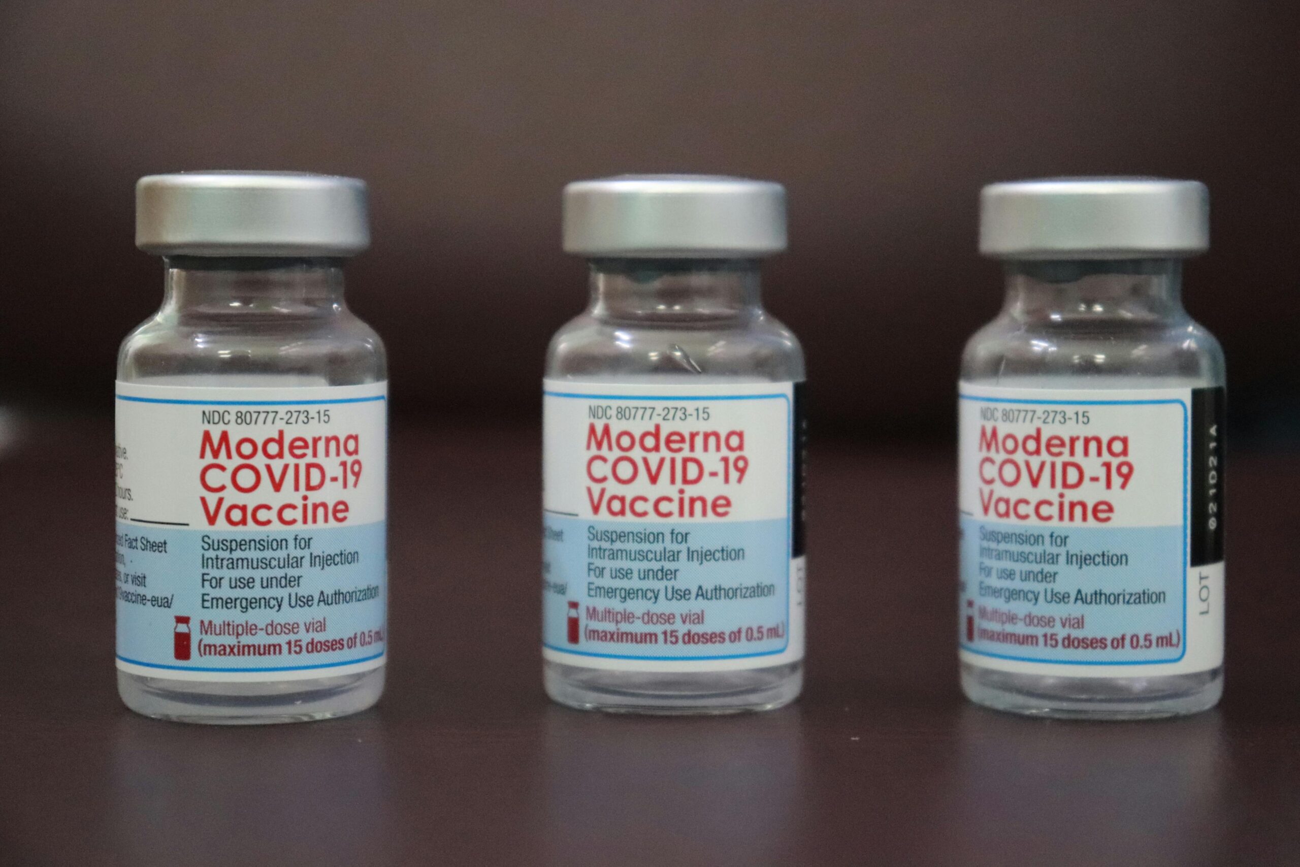 Close-up shot of three Moderna COVID-19 vaccine vials arranged against a dark background.