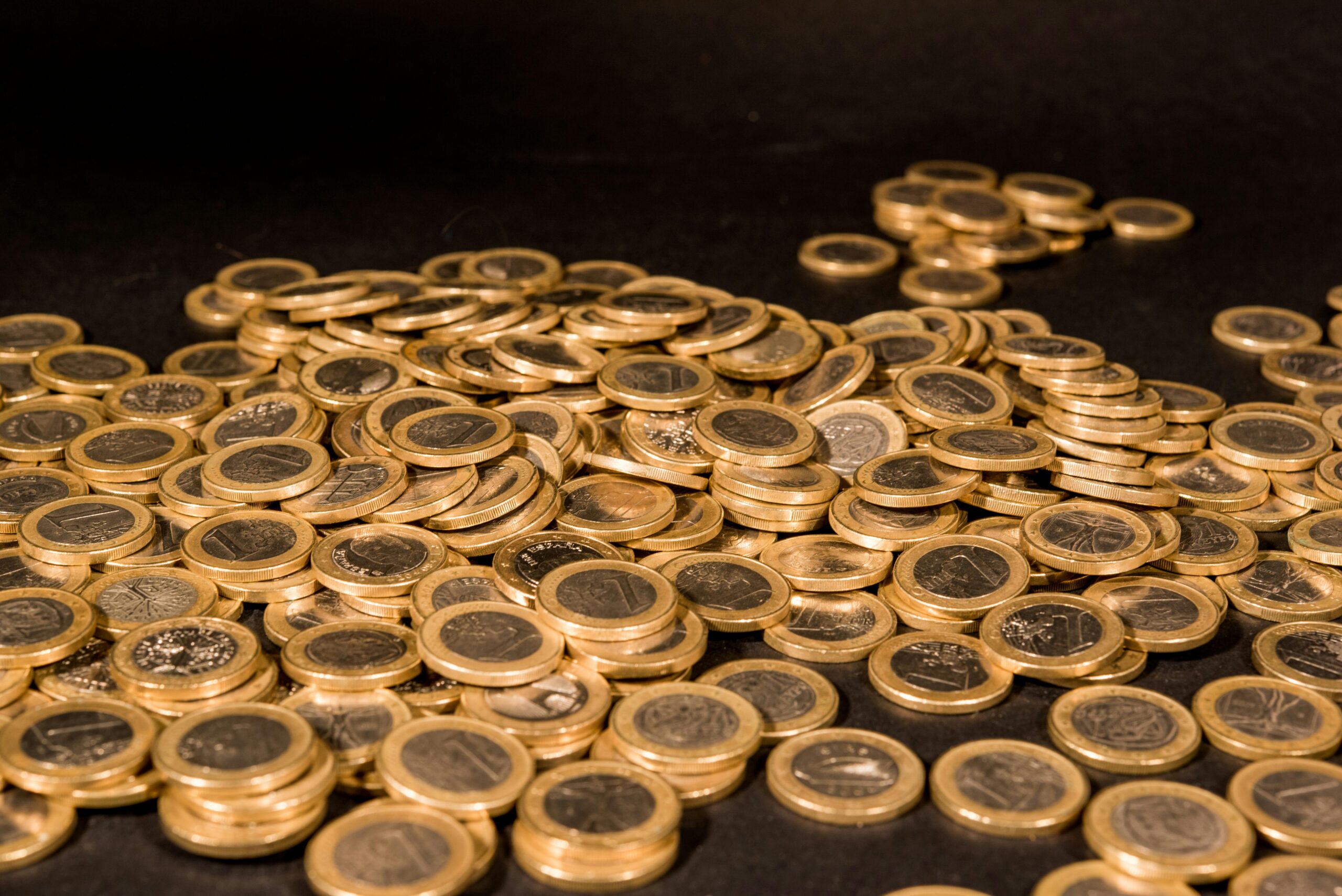 Close-up of a pile of Euro coins scattered on a black surface, representing wealth and finance.