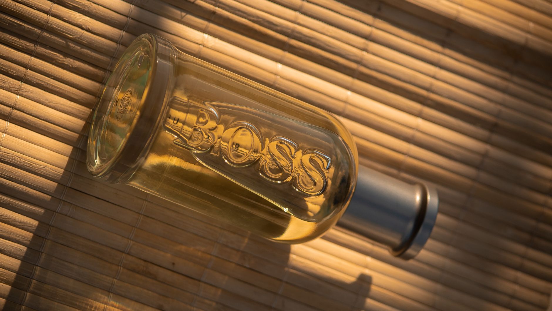 A stylish glass perfume bottle marked 'Boss' placed on a bamboo mat with sunlight highlighting its elegance.