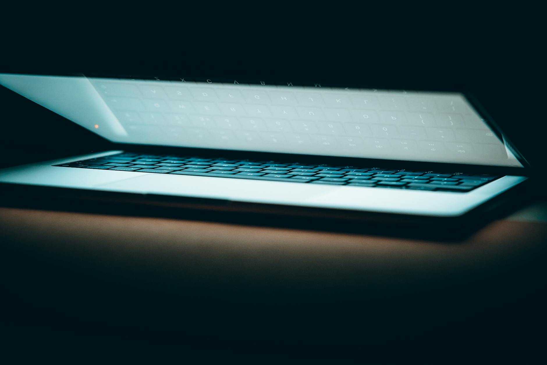 A close-up of a partially open laptop on a wooden surface, displayed in a moody lighting.