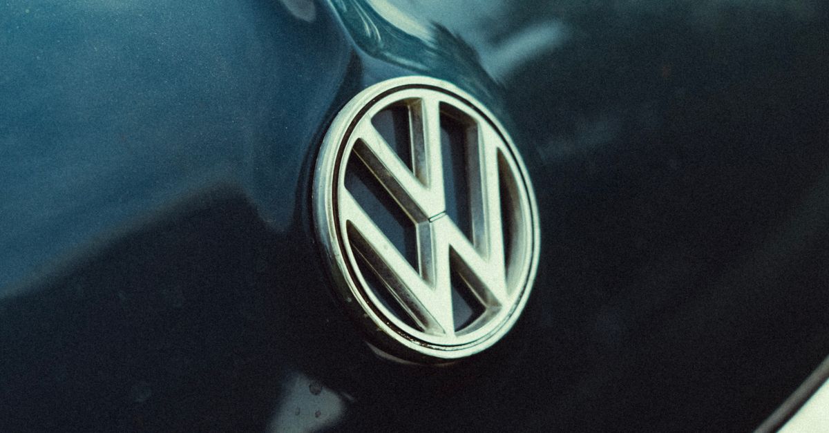 Vertical shot of Volkswagen logo on car hood with reflections of sky and trees.
