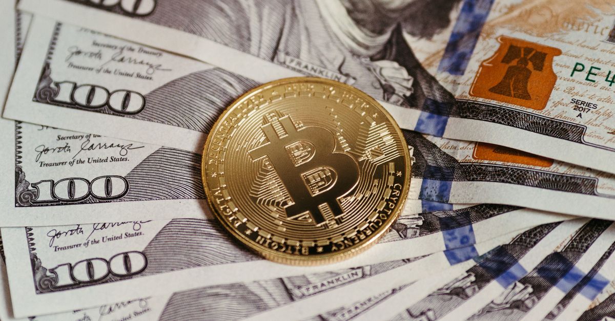Gold Bitcoin coin resting on US dollar bills showcasing digital and traditional currency.