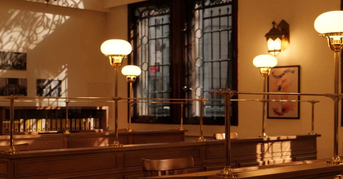 Sunlit vintage bank interior featuring wooden desks, chandeliers, and large windows.
