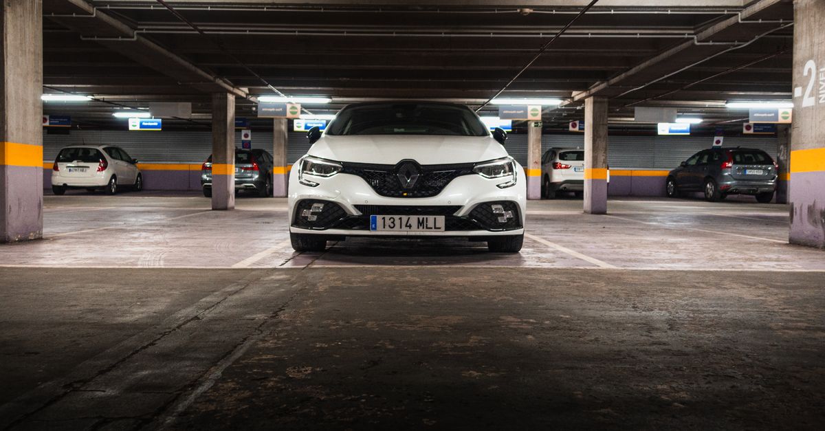 White Renault car in an underground parking garage with multiple vehicles visible.