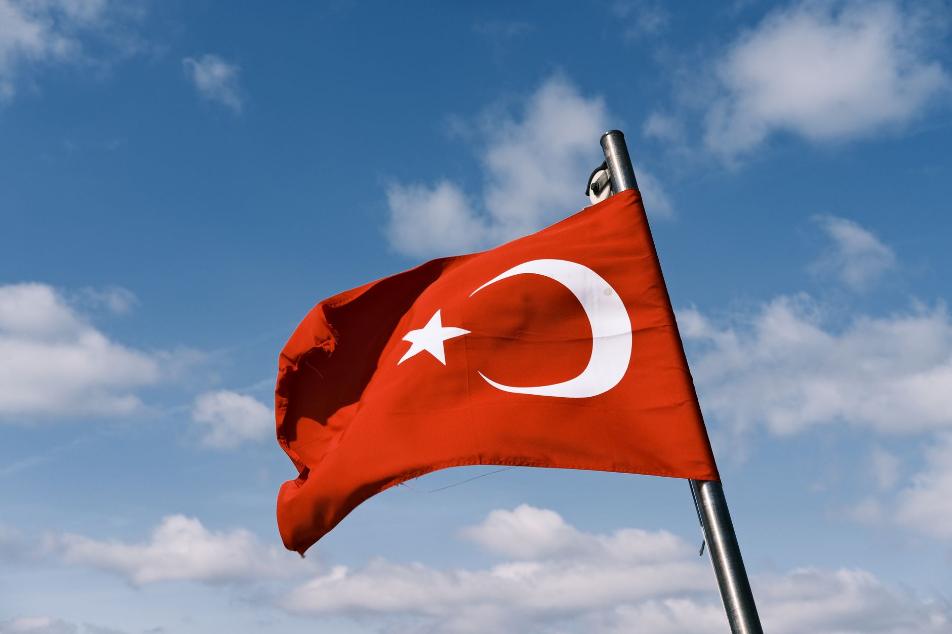 Turkish flag fluttering in the wind on a flagpole with a clear blue sky backdrop.