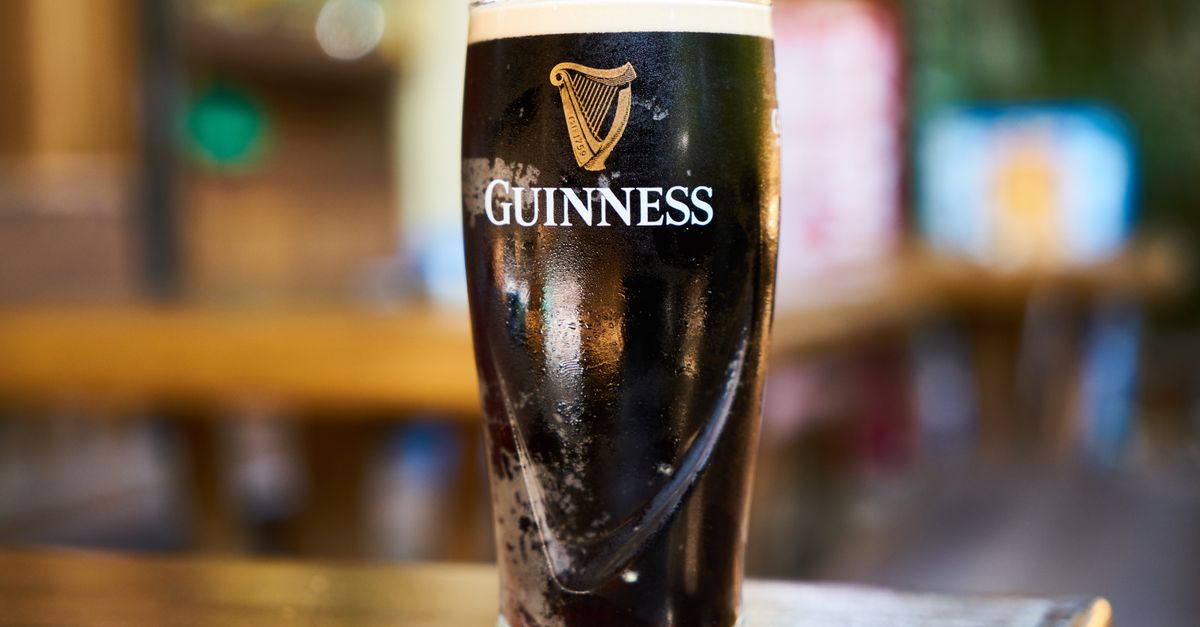 Close-up of a pint of Guinness stout beer on a wooden table in an indoor setting.