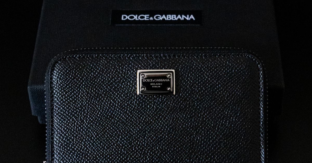 Elegant black designer wallet showcased with brand packaging in a dark setting.