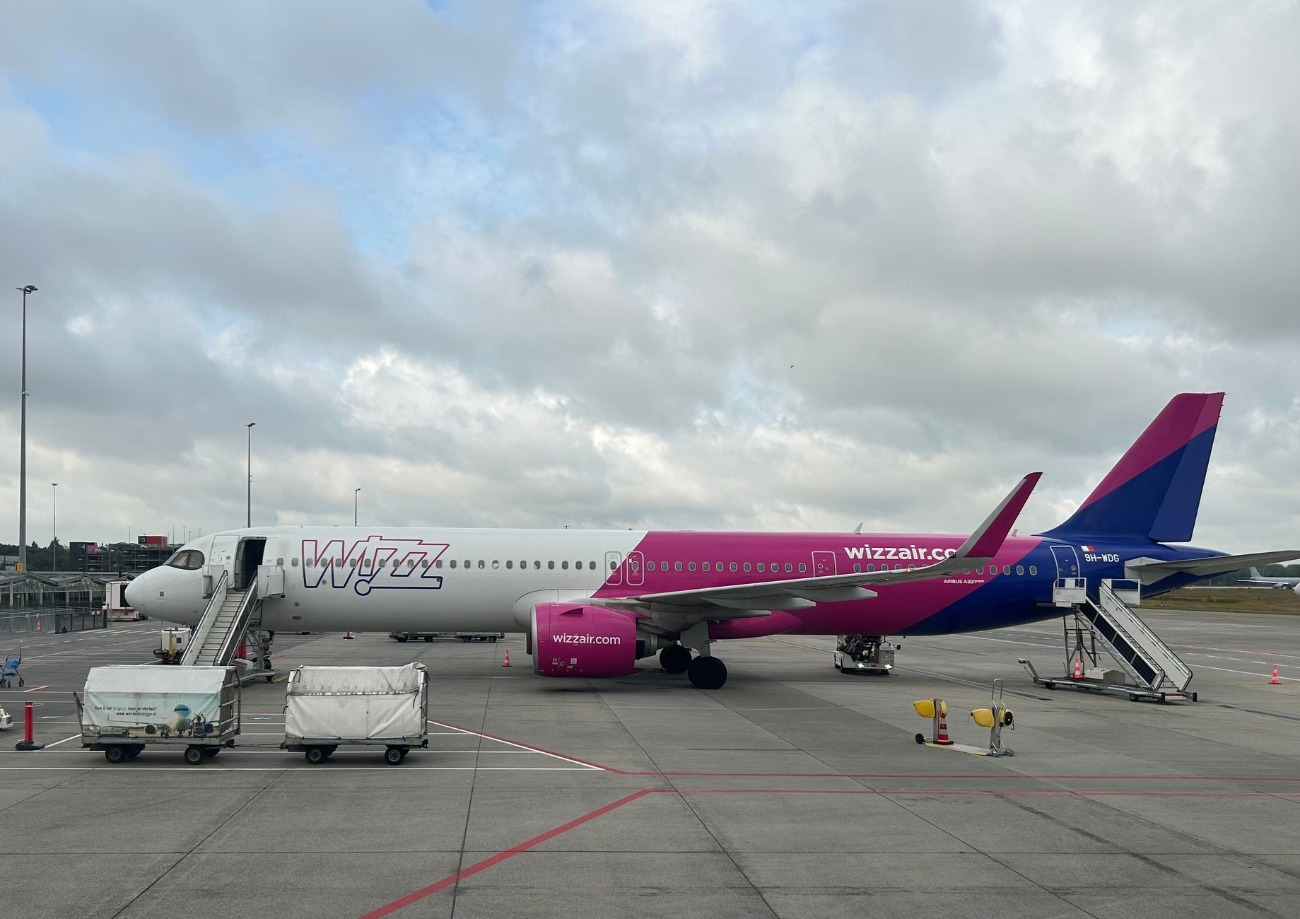 Wizz Air aircraft on tarmac with cloudy sky backdrop.