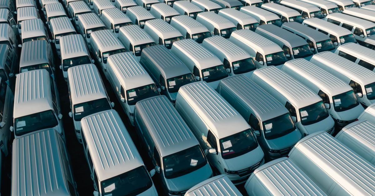 Aerial shot of multiple white vans parked in orderly rows in a lot under daylight.