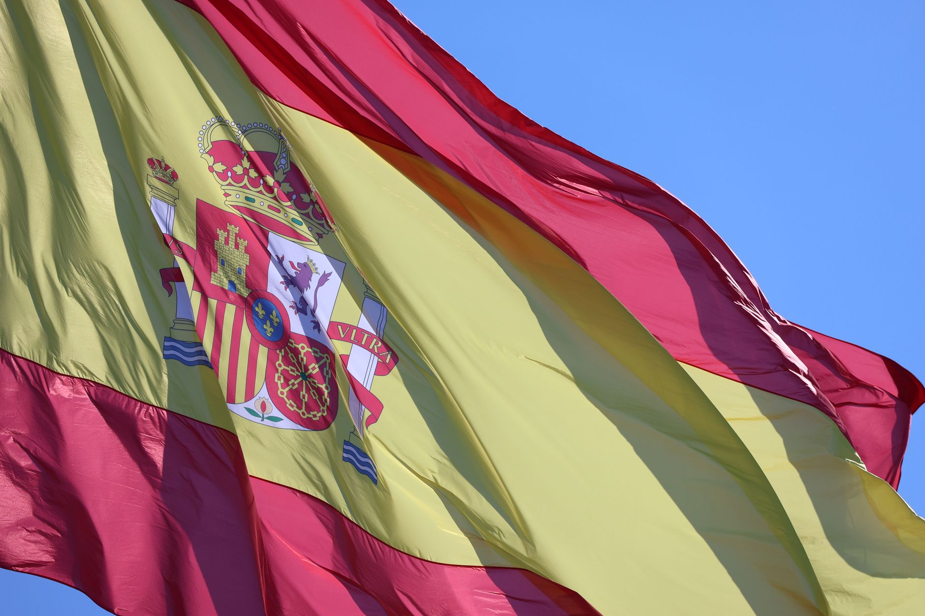 A vivid capture of the Spanish flag fluttering against a bright blue sky in Cádiz, Spain.