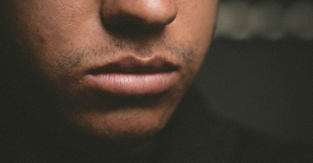 Detailed close-up of a man's lips and nose with textured skin, artistic lighting.