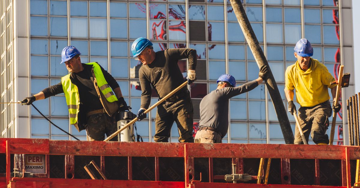 A group of construction workers in safety gear actively working on a high-rise building site.