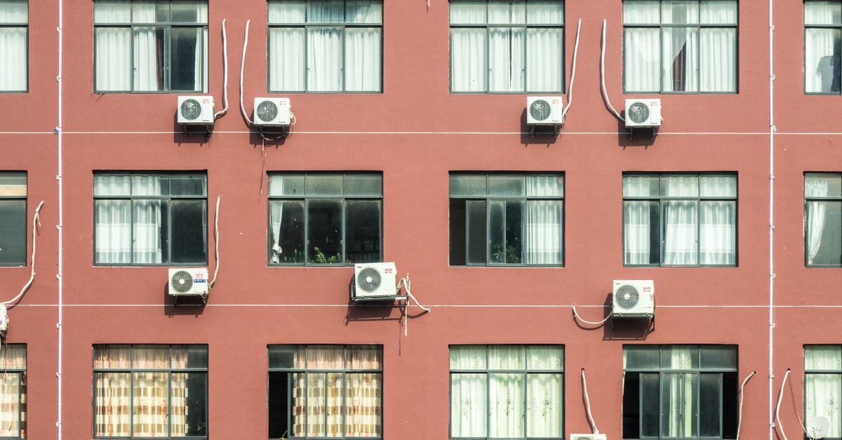 Red building exterior with multiple windows and air conditioners, showcasing urban architecture.
