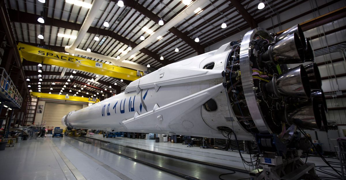 A SpaceX Falcon rocket displayed in a spacious hangar under bright industrial lights.