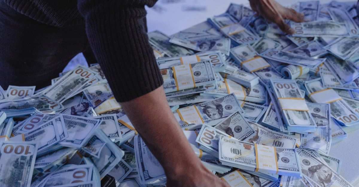Adult man organizing a massive pile of US dollar bills indoors in dynamic lighting.