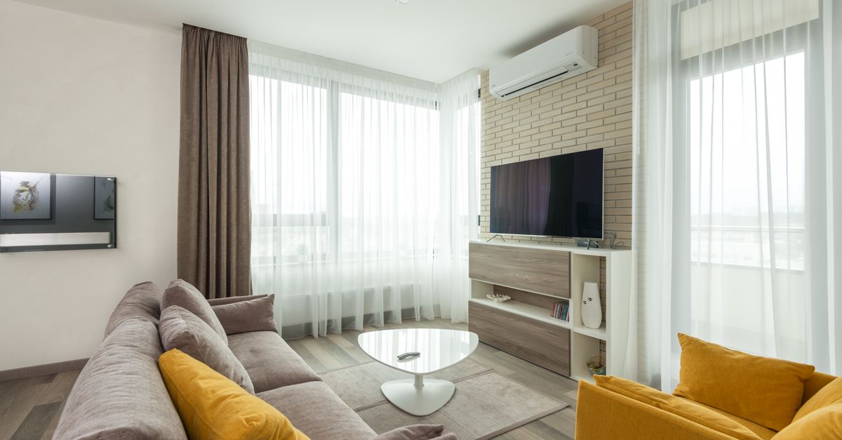 Soft comfortable sofa with cushions and armchair placed in front of TV hanging on brick wall in spacious living room of modern apartment