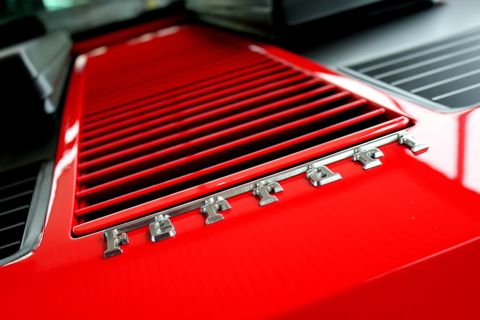 Detailed view of red Ferrari grille with metallic lettering, showcasing modern automotive design.