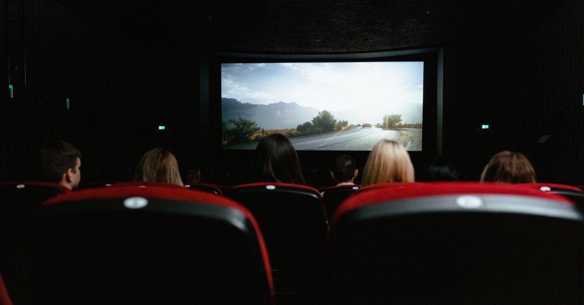 View from behind of people watching a movie in a cinema with red seats and a large screen.