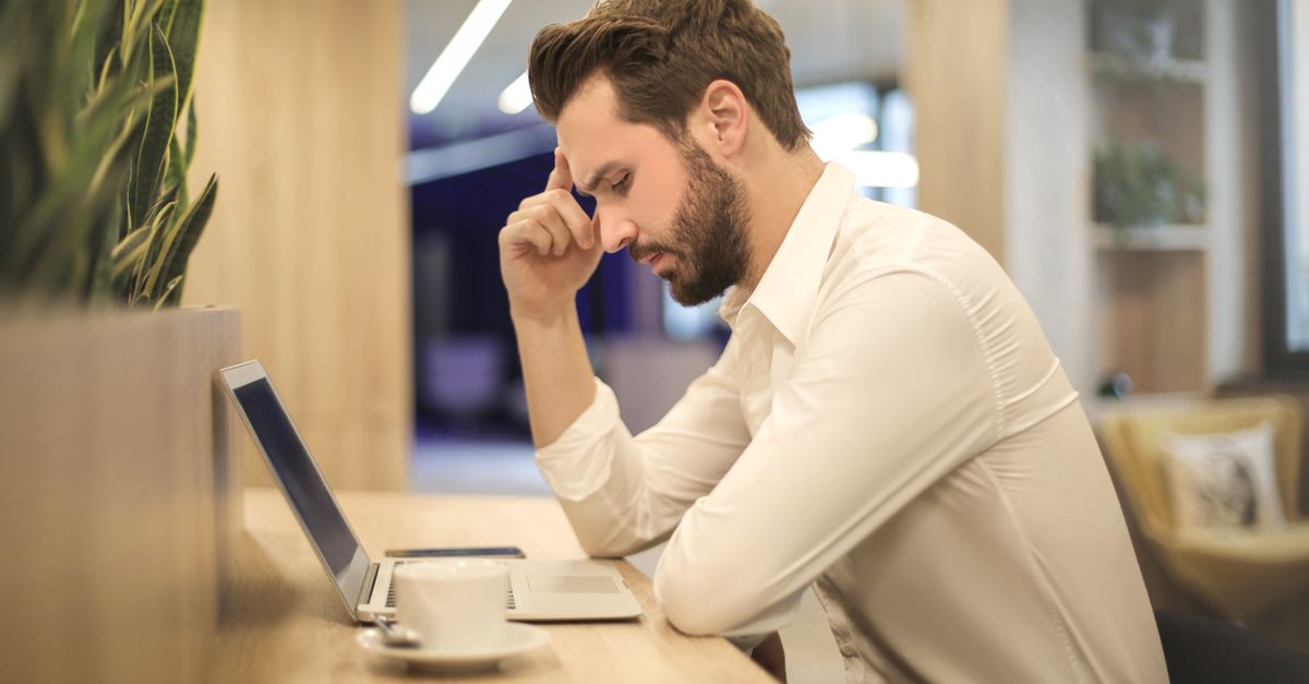 A thoughtful man in a shirt works on his laptop at a modern indoor office space.