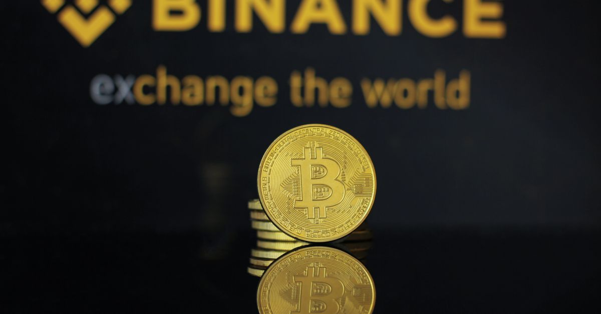Close-up of a Bitcoin coin with Binance logo and text reflecting in dark surface.