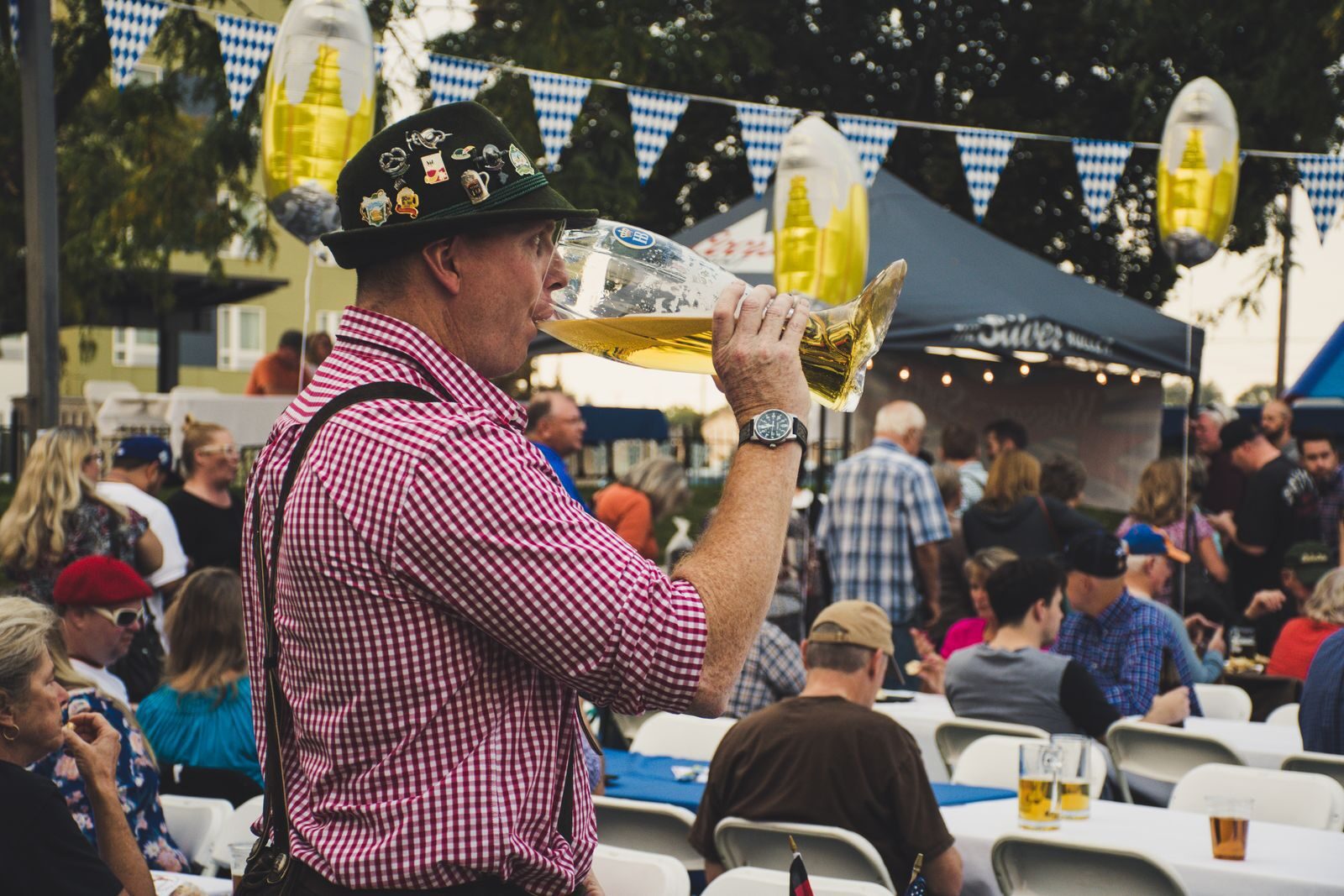 Man enjoying a large beer mug at an Oktoberfest celebration outdoors with a lively crowd.