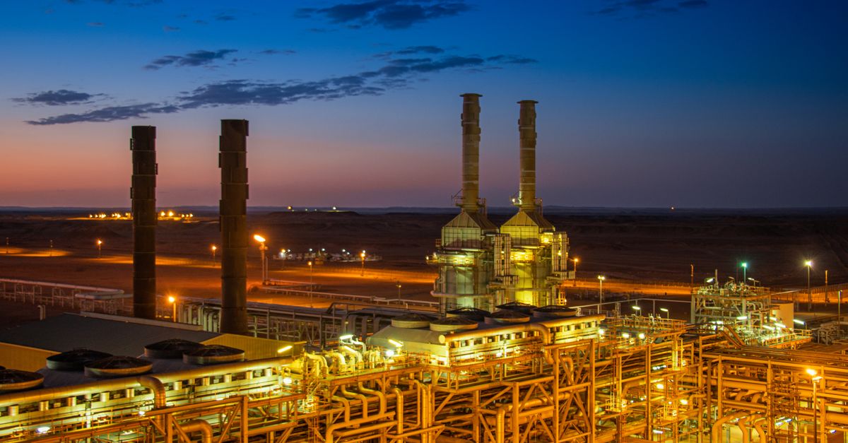 Aerial view of an illuminated factory with chimneys at sunset, showcasing industrial architecture.