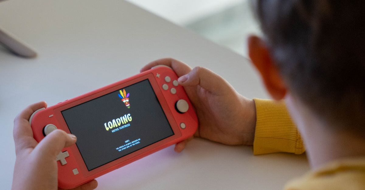 Child holding a pink handheld game console while a digital game loads on the screen.
