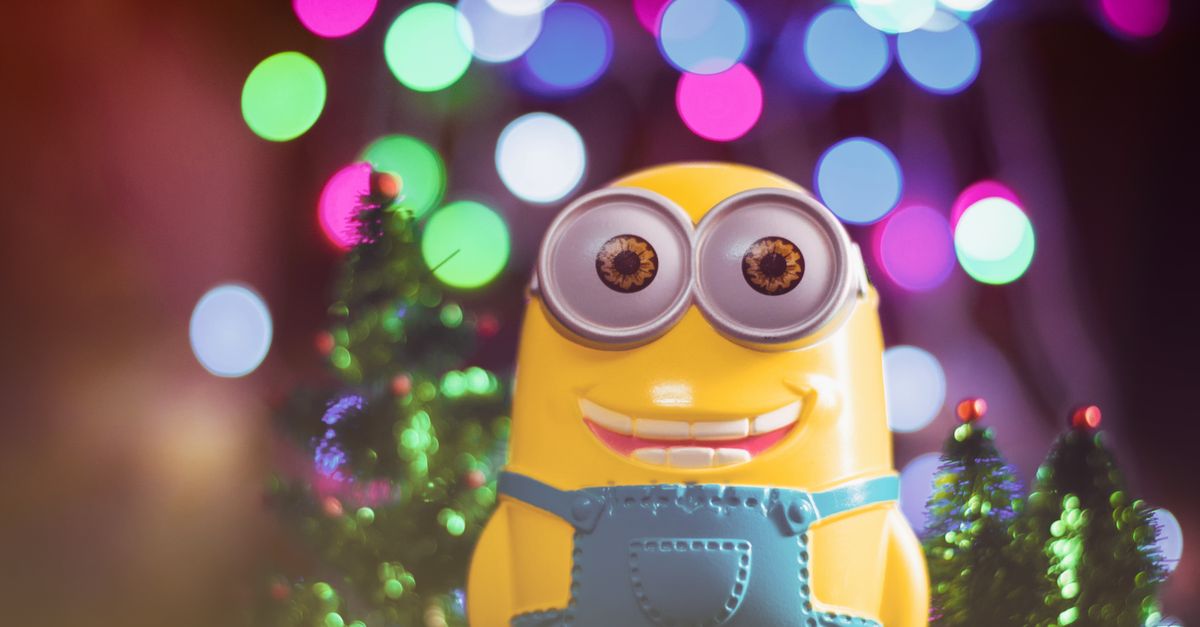 A cheerful minion toy among colorful bokeh lights and small Christmas trees.