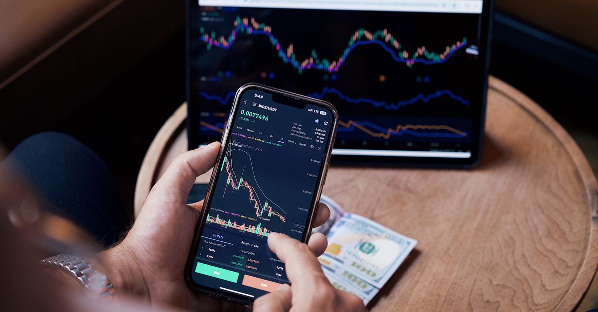 Close-up of a person trading stocks using a smartphone and a tablet.