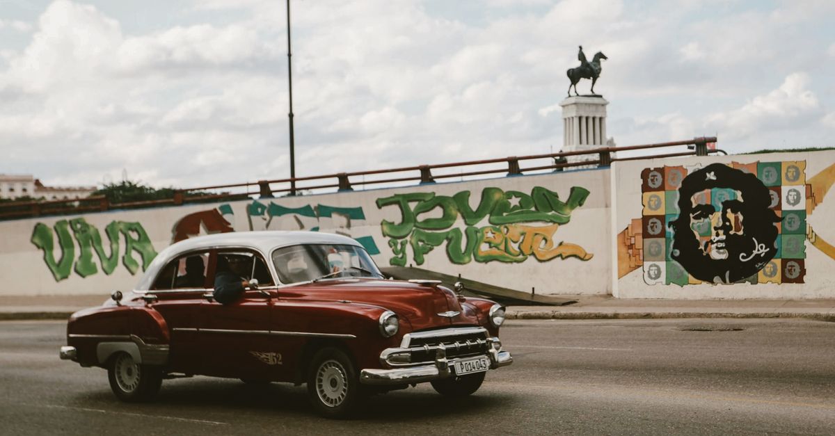 Classic Chevrolet car cruising past Havana street art with Che Guevara mural.