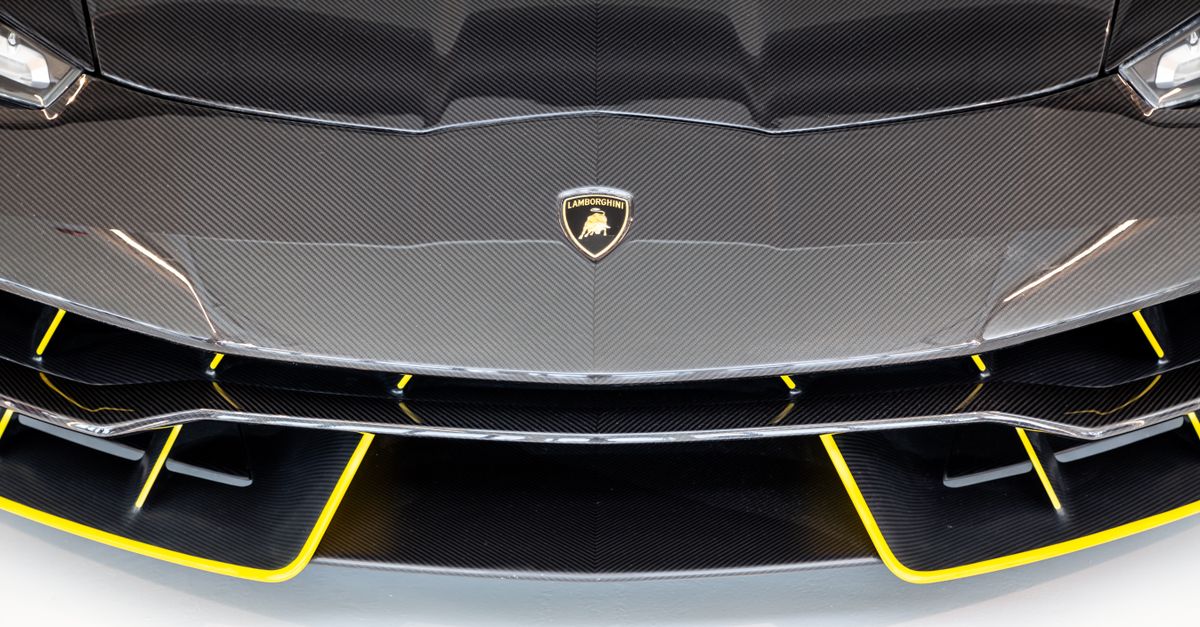 Close-up of a luxury sports car front, showcasing a sleek carbon fiber and yellow accented design.