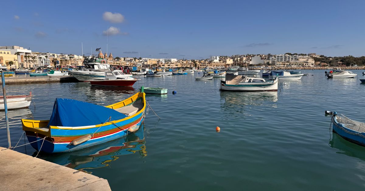 Vibrant traditional boats floating in the scenic Marsaxlokk harbor, Malta under a clear blue sky.