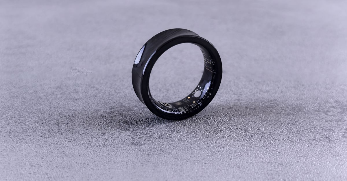 A modern black smart ring with visible circuitry resting on a textured concrete surface.