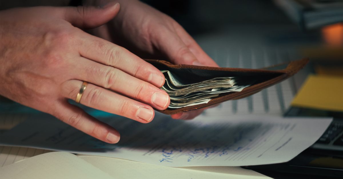 Hands holding an open wallet filled with cash above documents, indicating financial planning or budgeting.