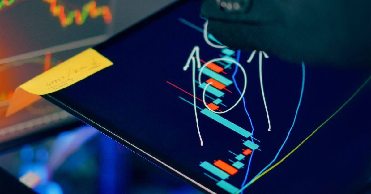 A business professional examines financial charts on a tablet and monitor for investment strategy.