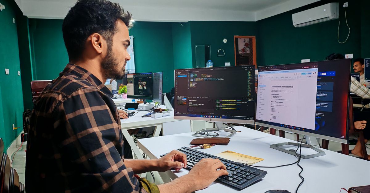 A software developer working on code at a dual monitor setup in a modern office.