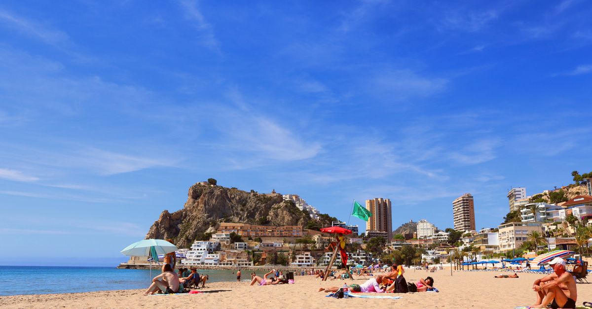 Relaxing beach in Alicante, vibrant day with clear blue skies and bustling city backdrop.