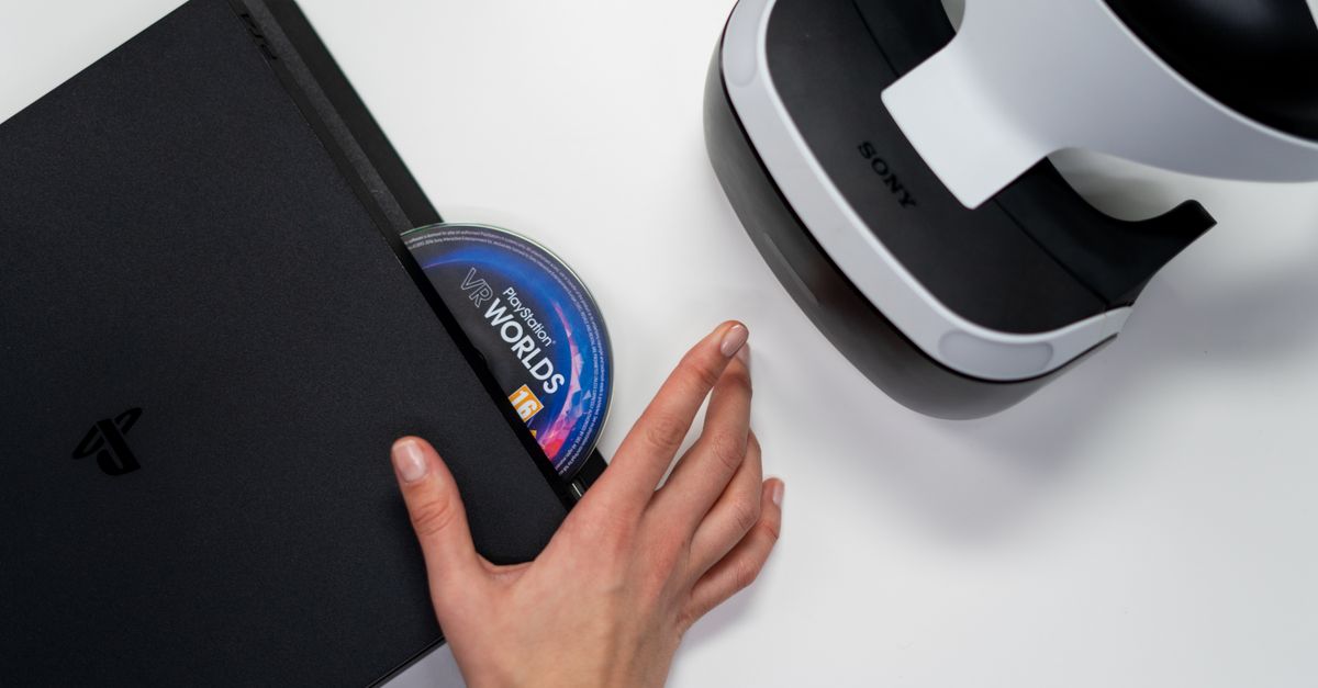 Close-up of a hand inserting a VR World's disc into a PlayStation with VR headset nearby.