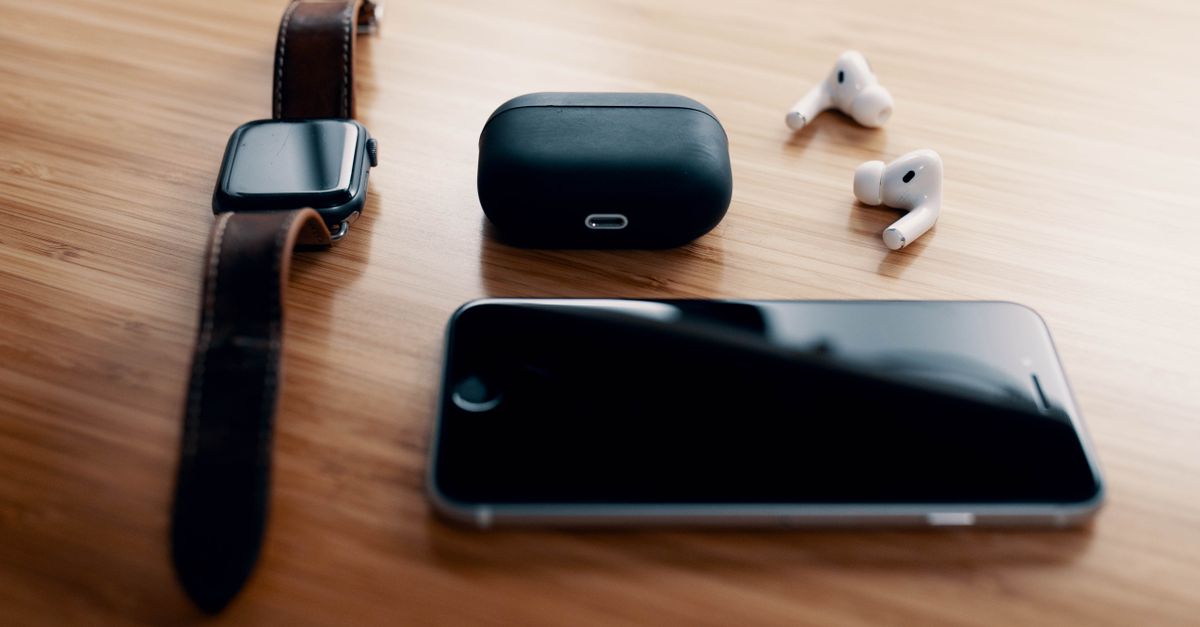Black smart watch and TWS earbuds with charging case and smartphone lying on wooden table