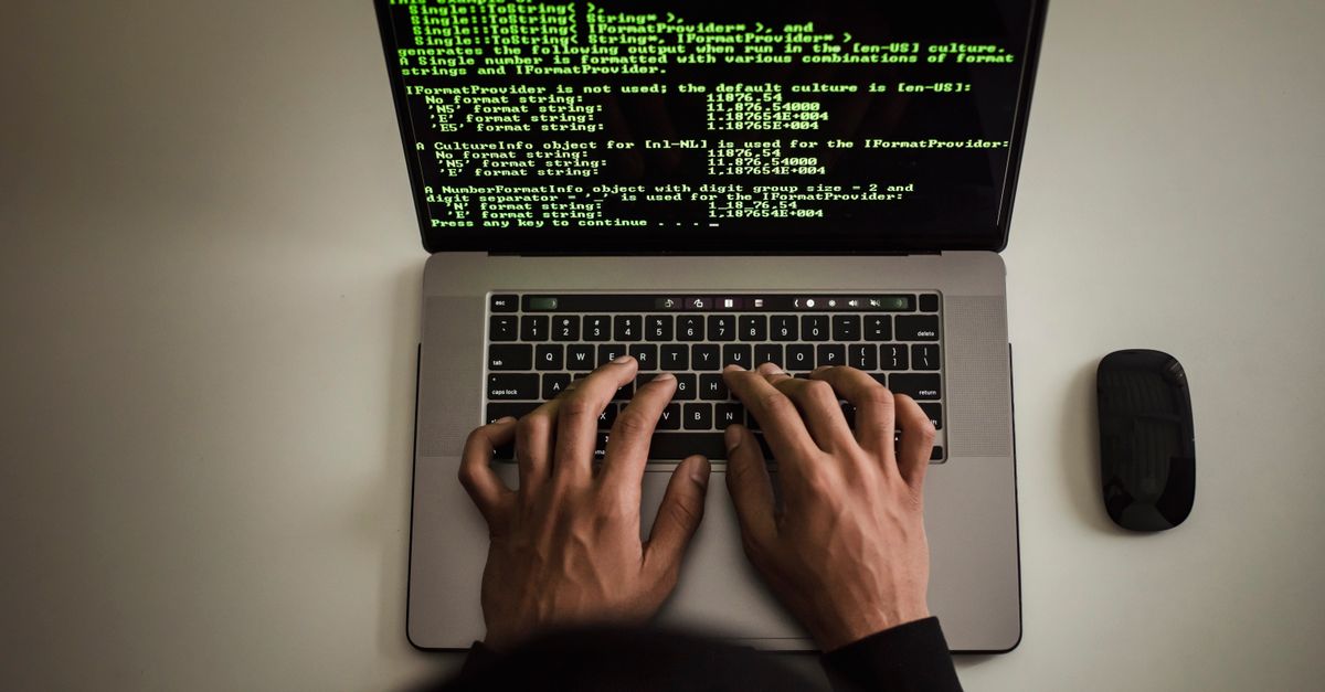From above crop anonymous male programmer in black hoodie working on software code on contemporary netbook and typing on keyboard in workspace