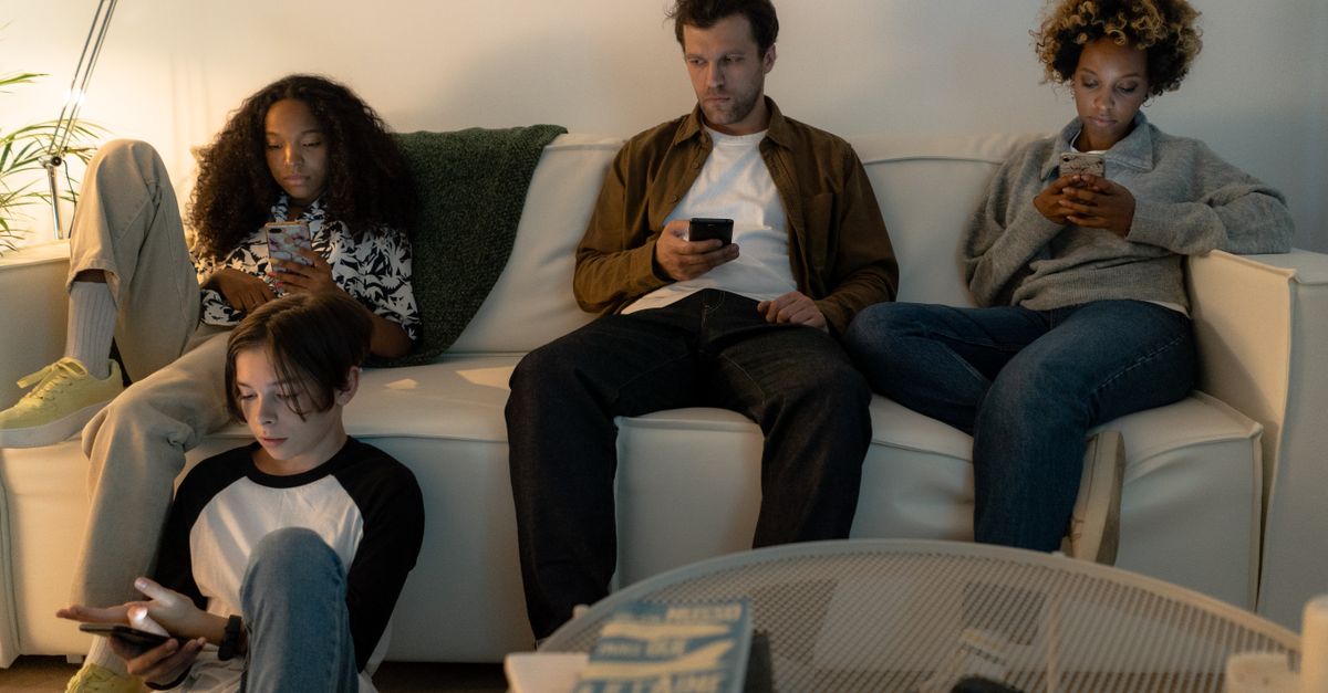 A diverse family sits on a sofa using their smartphones together indoors.